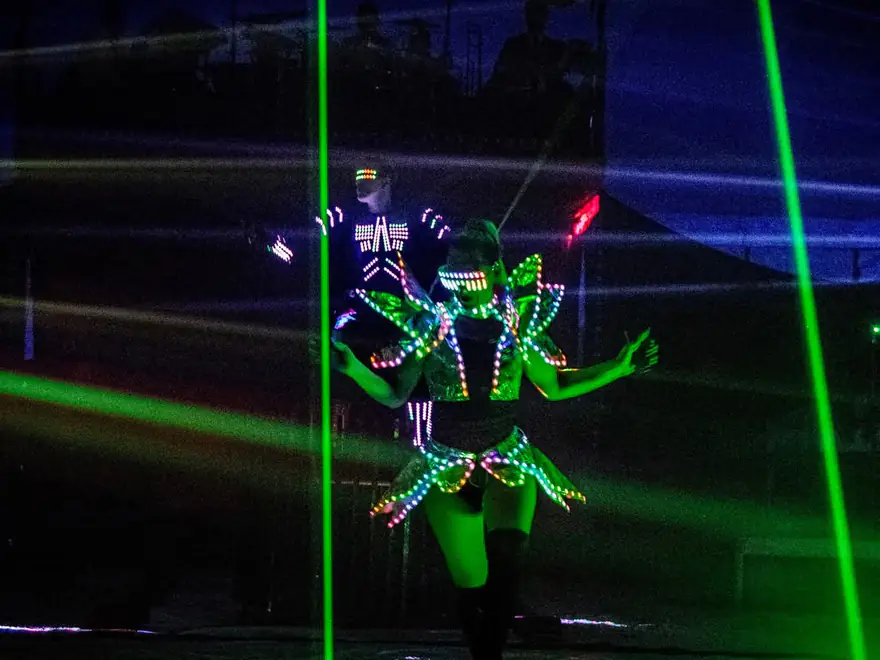 Een artiest in een LED-kostuum tussen groene laserstralen tijdens het lichtspektakel