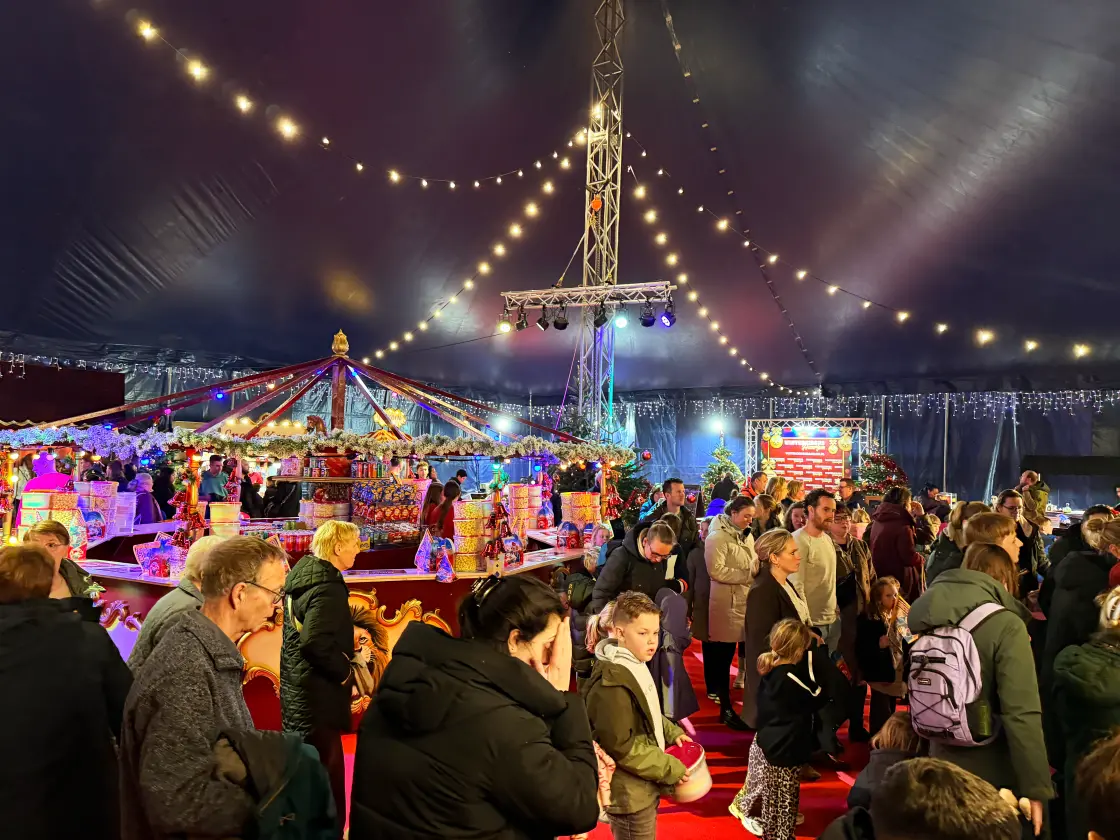 Bezoekers rond de draaimolen in de foyertent onder slingers van lampjes