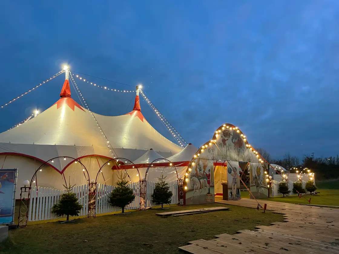 De verlichte circustenten bij schemering, met een pad langs kleine kerstboompjes naar de ingang